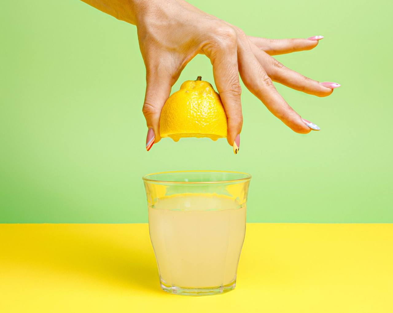 Dłoń wyciskająca połówkę cytryny nad szklanką lemoniady